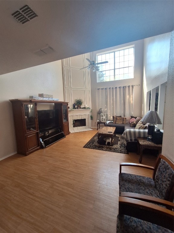 living room with ceiling fan, a tile fireplace, a high ceiling, and hardwood / wood-style floors