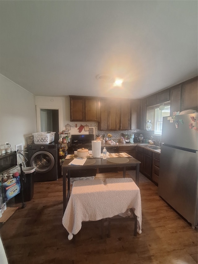 kitchen featuring washer / clothes dryer, range, hardwood / wood-style floors, stainless steel refrigerator, and tasteful backsplash