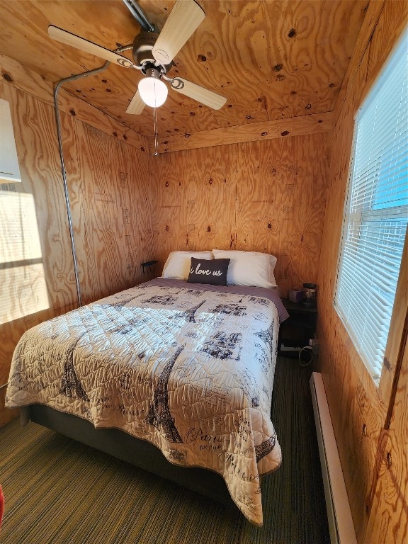 bedroom with wooden walls, multiple windows, a baseboard radiator, and ceiling fan