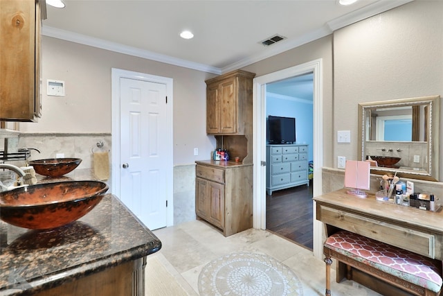 kitchen with light tile patterned floors, dark stone countertops, ornamental molding, and sink