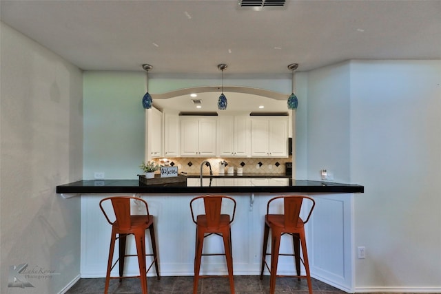 kitchen featuring a kitchen bar, decorative backsplash, kitchen peninsula, pendant lighting, and white cabinets