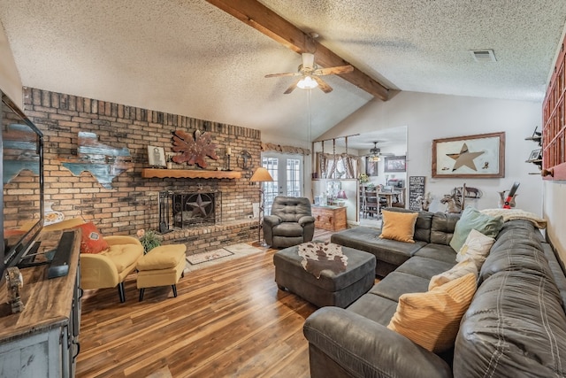 living room featuring vaulted ceiling with beams, dark hardwood / wood-style floors, ceiling fan, a brick fireplace, and a textured ceiling