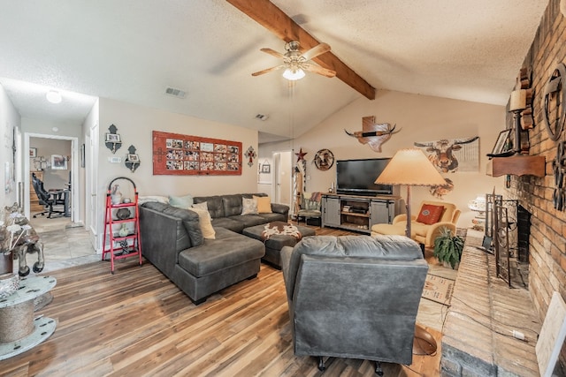 living room with a brick fireplace, a textured ceiling, ceiling fan, and light wood-type flooring