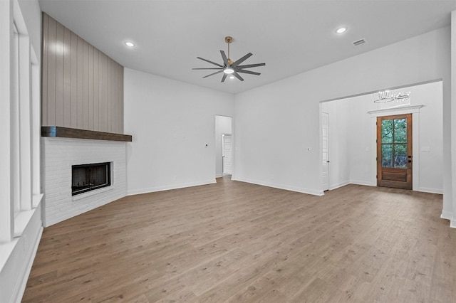 unfurnished living room featuring ceiling fan with notable chandelier, light hardwood / wood-style floors, and a brick fireplace