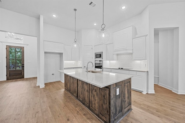 kitchen featuring white cabinets, a center island with sink, light hardwood / wood-style flooring, and stainless steel appliances