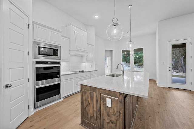 kitchen with sink, white cabinets, light hardwood / wood-style floors, and a center island with sink