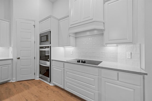 kitchen with black electric stovetop, light hardwood / wood-style floors, white cabinetry, and stainless steel microwave