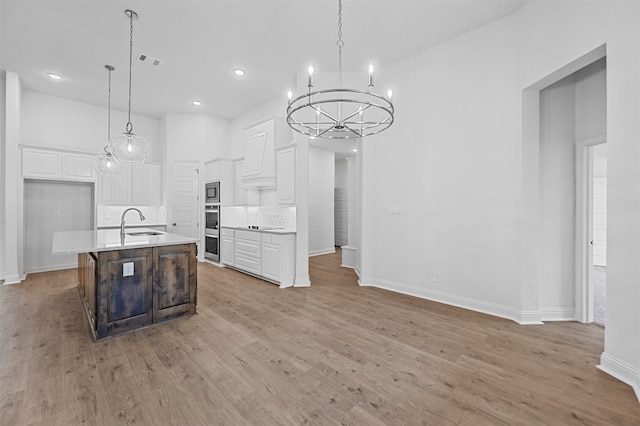 kitchen featuring decorative light fixtures, a center island with sink, white cabinetry, and sink