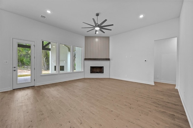 unfurnished living room featuring ceiling fan, a large fireplace, and light hardwood / wood-style flooring