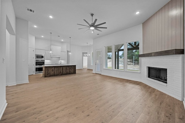 unfurnished living room with sink, a fireplace, ceiling fan with notable chandelier, and light wood-type flooring