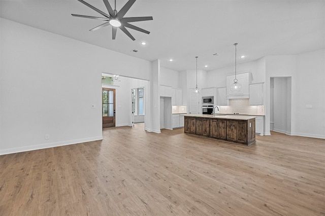 kitchen featuring stainless steel appliances, pendant lighting, light hardwood / wood-style floors, white cabinetry, and an island with sink