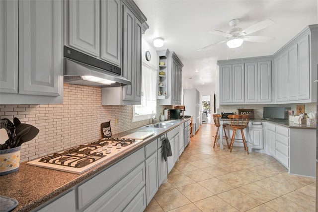 kitchen with gray cabinetry, backsplash, ceiling fan, light tile floors, and white gas stovetop