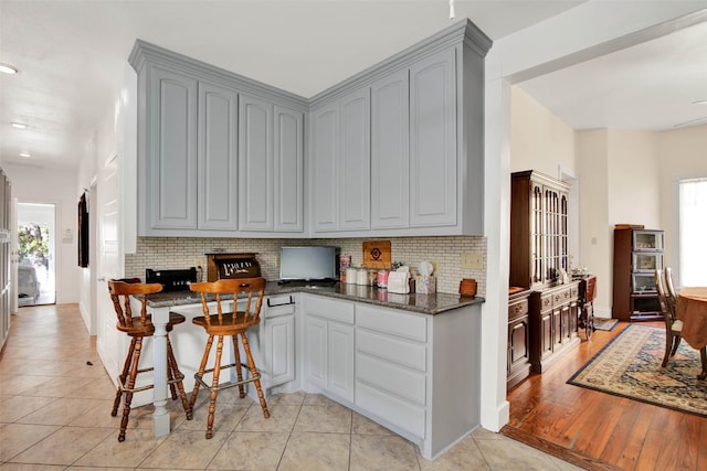 kitchen with backsplash, light hardwood / wood-style floors, gray cabinets, and dark stone counters