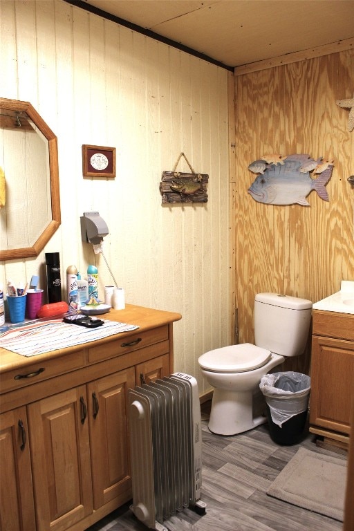 bathroom with toilet, wood walls, hardwood / wood-style flooring, vanity, and radiator heating unit