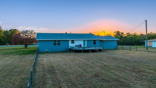 back house at dusk featuring a deck, central air condition unit, and a lawn