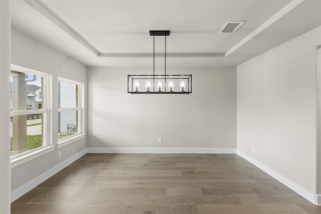 unfurnished dining area featuring wood-type flooring, a chandelier, and a raised ceiling