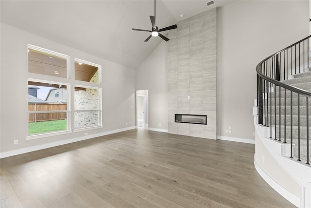 unfurnished living room with a tile fireplace, hardwood / wood-style floors, ceiling fan, and high vaulted ceiling