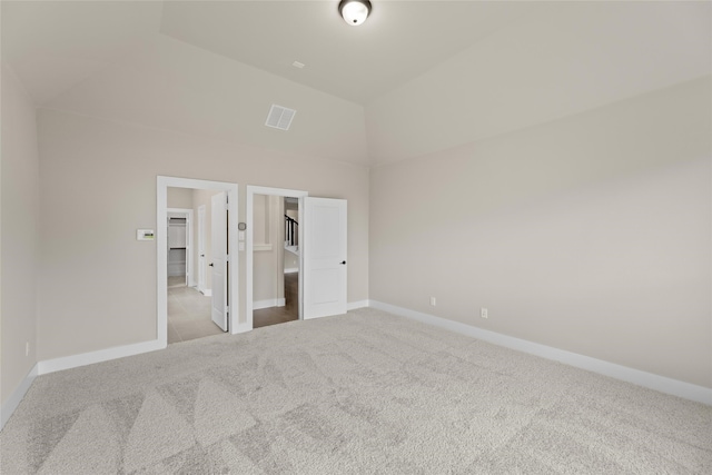 unfurnished bedroom with ensuite bath, a spacious closet, vaulted ceiling, and light carpet