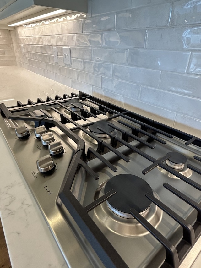 details featuring stainless steel gas stovetop, range, and tasteful backsplash