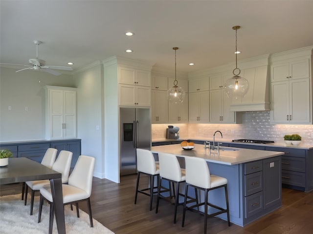 kitchen with a kitchen island with sink, stainless steel fridge with ice dispenser, custom exhaust hood, gas cooktop, and a sink