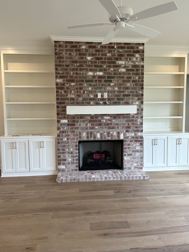 unfurnished living room featuring a fireplace, wood finished floors, built in shelves, and ornamental molding