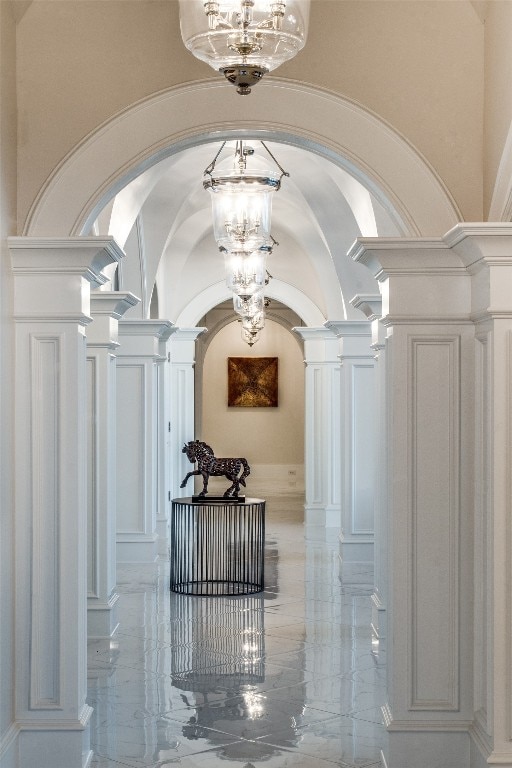 corridor with light tile flooring, a chandelier, vaulted ceiling, and decorative columns