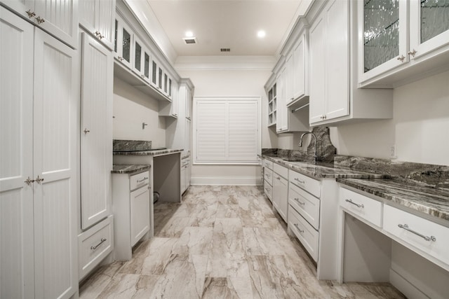 kitchen with dark stone countertops, white cabinets, light tile floors, and sink