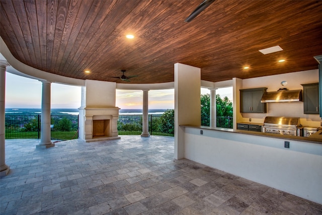 kitchen featuring ceiling fan, a large fireplace, wooden ceiling, wall chimney range hood, and dark tile flooring