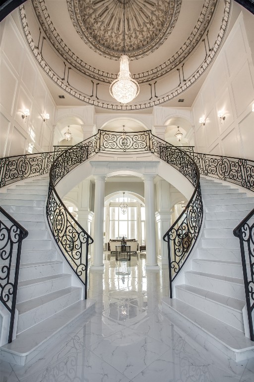 stairway with a towering ceiling, tile floors, a chandelier, and ornate columns