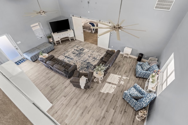 living room with ceiling fan, light wood-type flooring, and a high ceiling