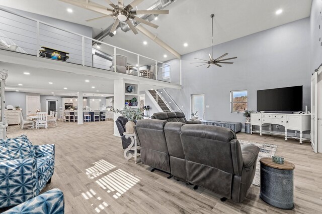 living room with ceiling fan, light hardwood / wood-style flooring, and a high ceiling