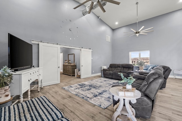 living room with ceiling fan, light wood-type flooring, high vaulted ceiling, and a barn door