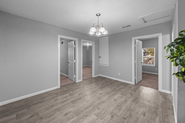 unfurnished room with an inviting chandelier, light hardwood / wood-style flooring, and a textured ceiling