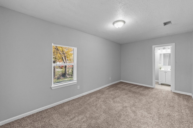 unfurnished bedroom with ensuite bathroom, carpet, and a textured ceiling