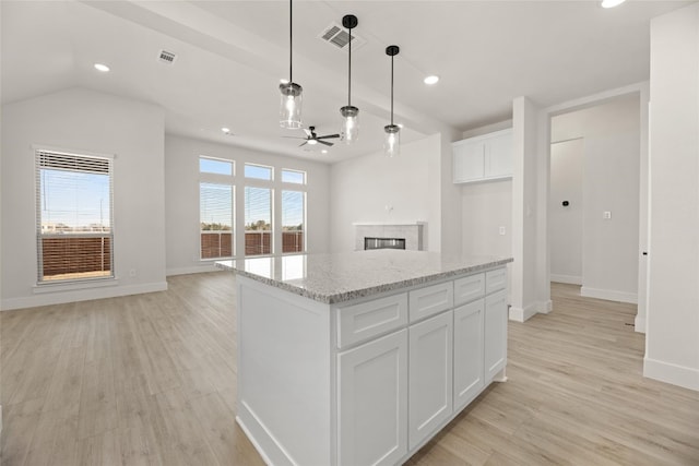 kitchen with light stone counters, hanging light fixtures, light wood-type flooring, white cabinets, and a center island