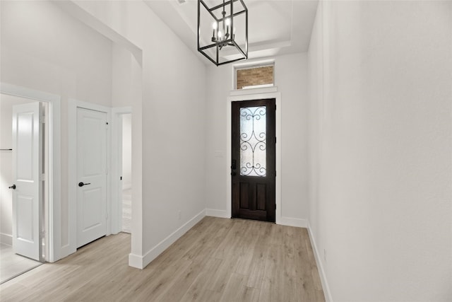 foyer with an inviting chandelier, a tray ceiling, and light hardwood / wood-style floors