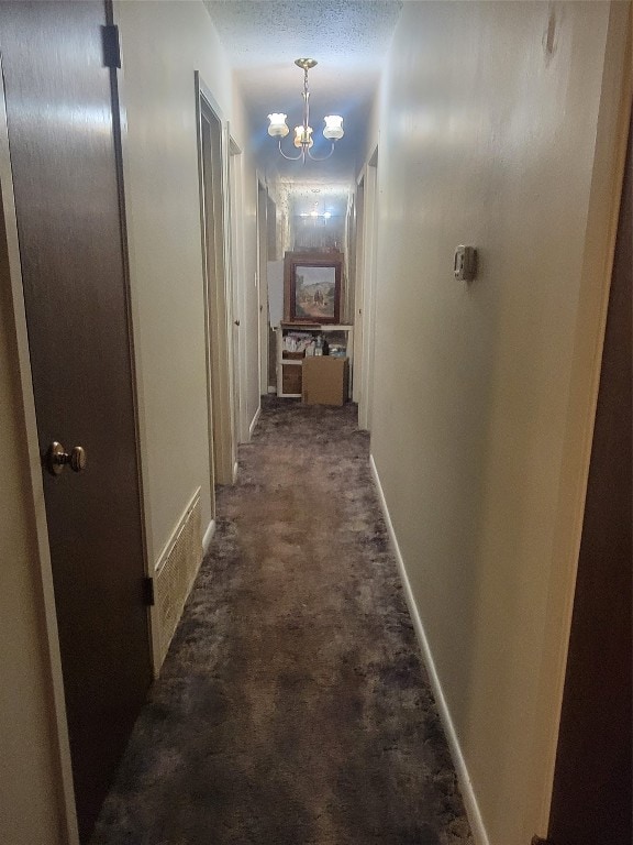 hallway featuring an inviting chandelier, a textured ceiling, and dark carpet