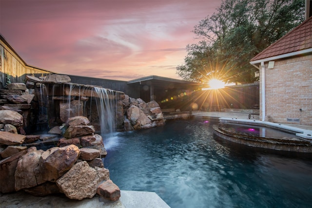 pool at dusk featuring pool water feature and an in ground hot tub