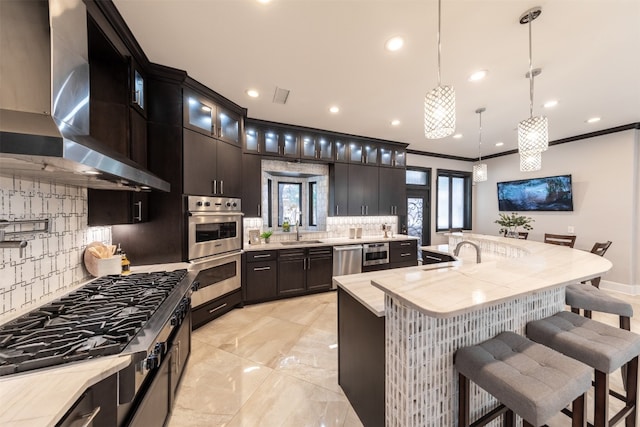 kitchen featuring a kitchen island with sink, stainless steel appliances, ornamental molding, decorative light fixtures, and exhaust hood