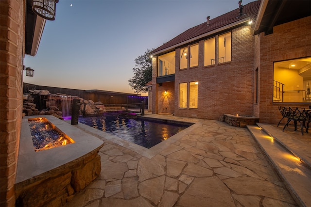 pool at dusk featuring a patio area, pool water feature, and an outdoor fire pit