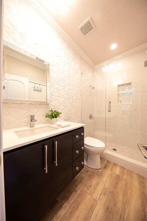 bathroom with wood-type flooring, ornamental molding, vanity, walk in shower, and toilet