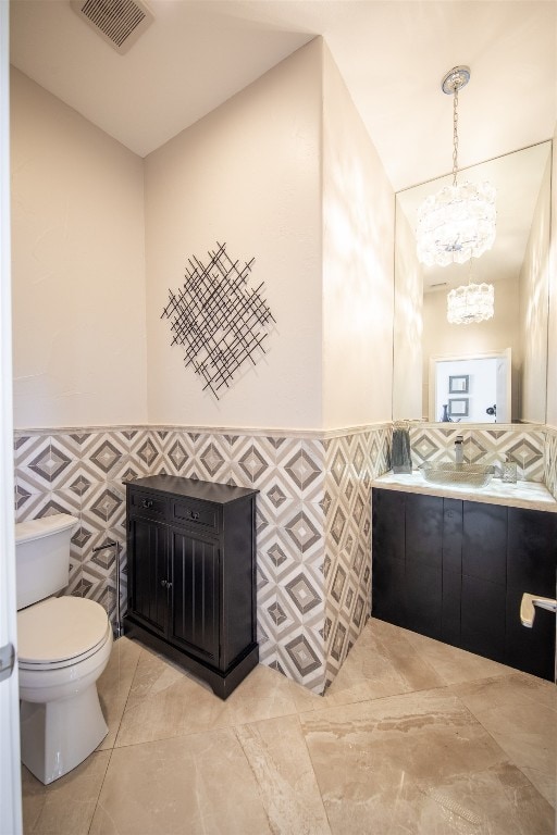 bathroom with vanity, toilet, tile walls, and an inviting chandelier