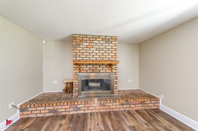 unfurnished living room with dark wood-type flooring, a fireplace, and brick wall