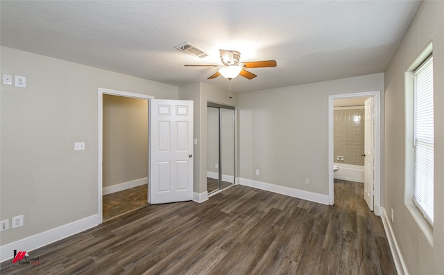 unfurnished bedroom featuring ceiling fan, dark hardwood / wood-style floors, ensuite bath, and a closet