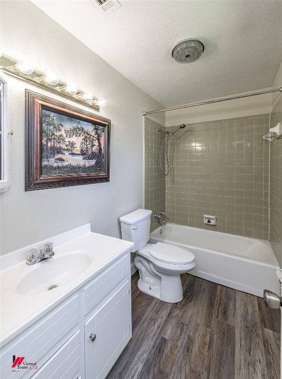 full bathroom with a textured ceiling, toilet, vanity, hardwood / wood-style flooring, and tiled shower / bath