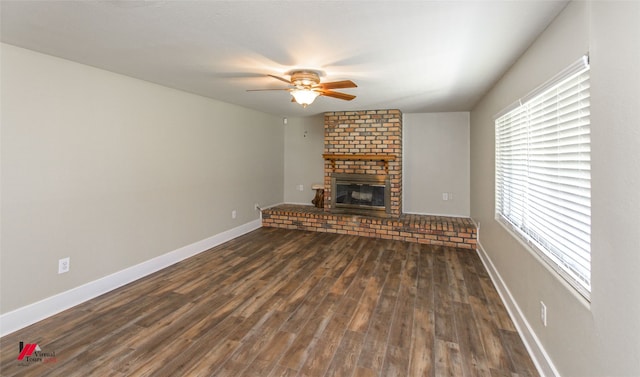 unfurnished living room featuring dark hardwood / wood-style flooring, ceiling fan, brick wall, and a fireplace