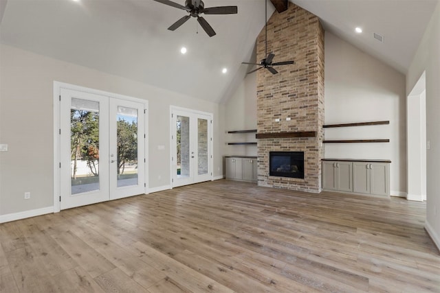 unfurnished living room with french doors, a brick fireplace, ceiling fan, light hardwood / wood-style floors, and high vaulted ceiling