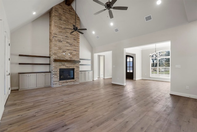 unfurnished living room with brick wall, light hardwood / wood-style flooring, a fireplace, high vaulted ceiling, and ceiling fan with notable chandelier