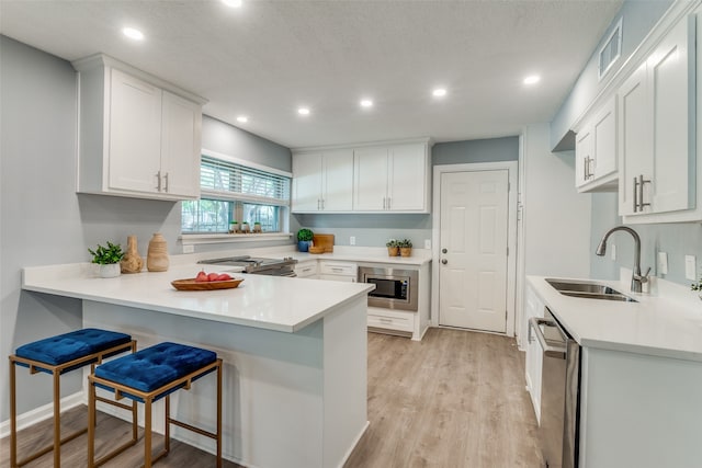 kitchen featuring appliances with stainless steel finishes, light hardwood / wood-style flooring, white cabinets, a breakfast bar, and sink