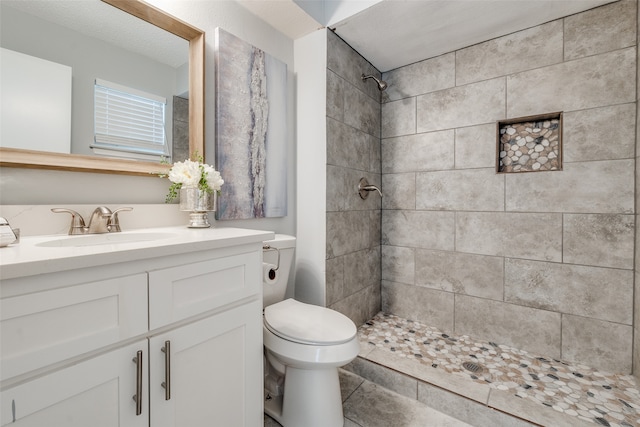 bathroom with tile patterned floors, toilet, vanity, and a tile shower